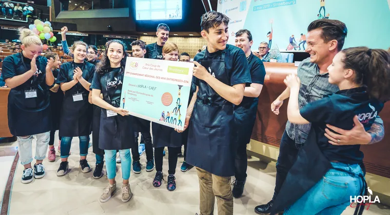 Remise de prix Hopla Chef dans l'hémicycle du Conseil de l'Europe à Strasbourg : un jeune reçoit son prix, l'équipe applaudit.