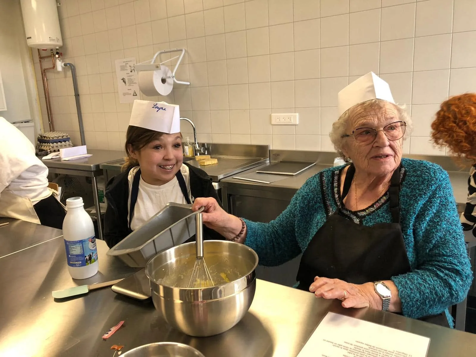 Une jeune fille et une personne âgée préparent une recette ensemble lors d'une rencontre Hopla Chef.