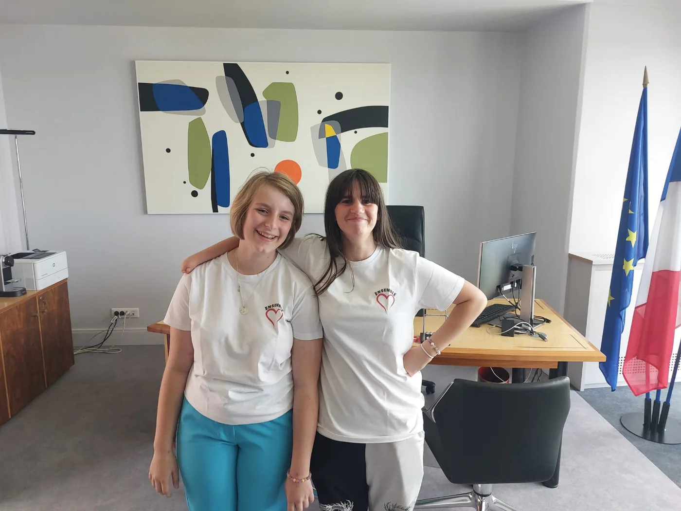 Deux jeunes reporters dans le bureau d’un élu, drapeaux français et européen en arrière-plan.