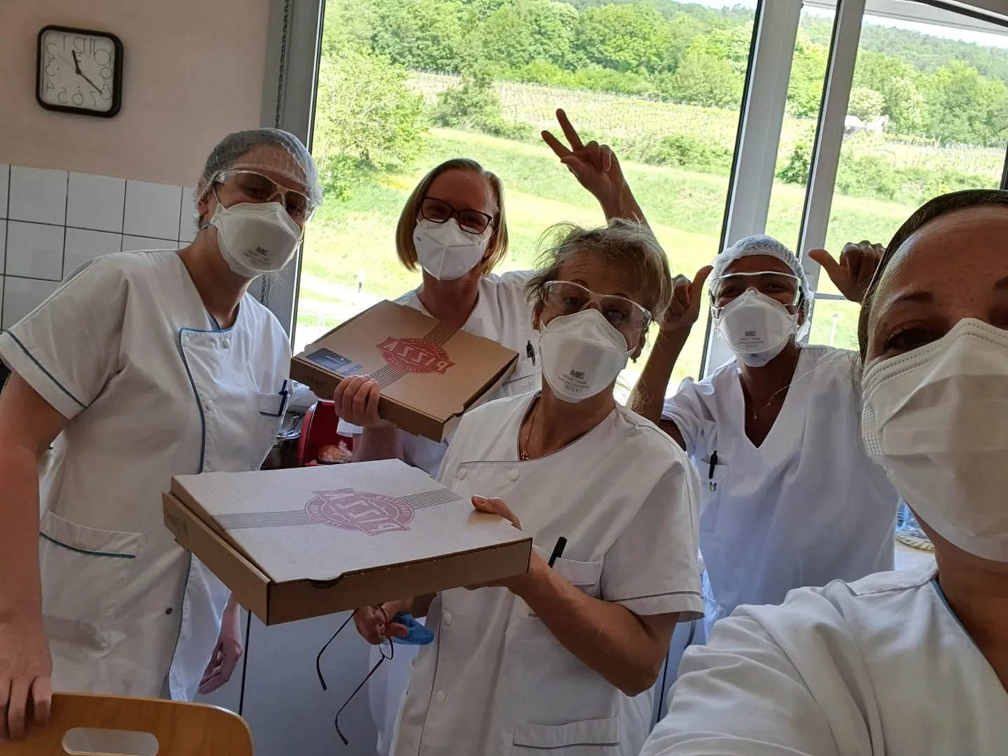 Des soignants masqués forment un cœur avec leurs mains, derrière des boîtes de pizzas offertes par l’association.