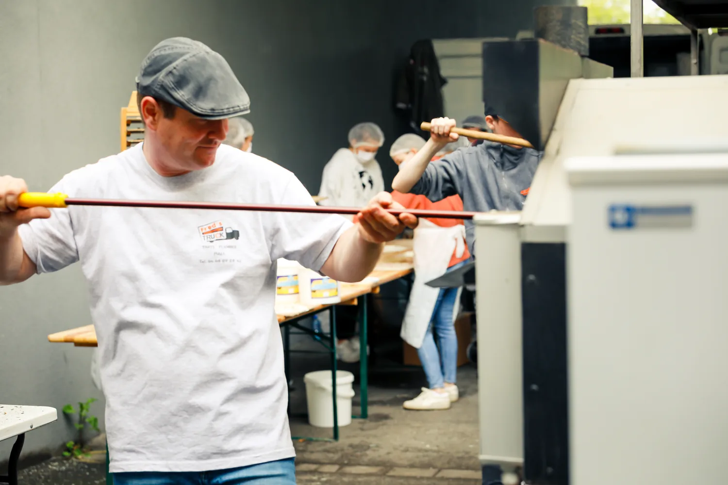 Un bénévole enfourne une tarte flambée dans le four à bois installé pour l’hôpital de Haguenau.