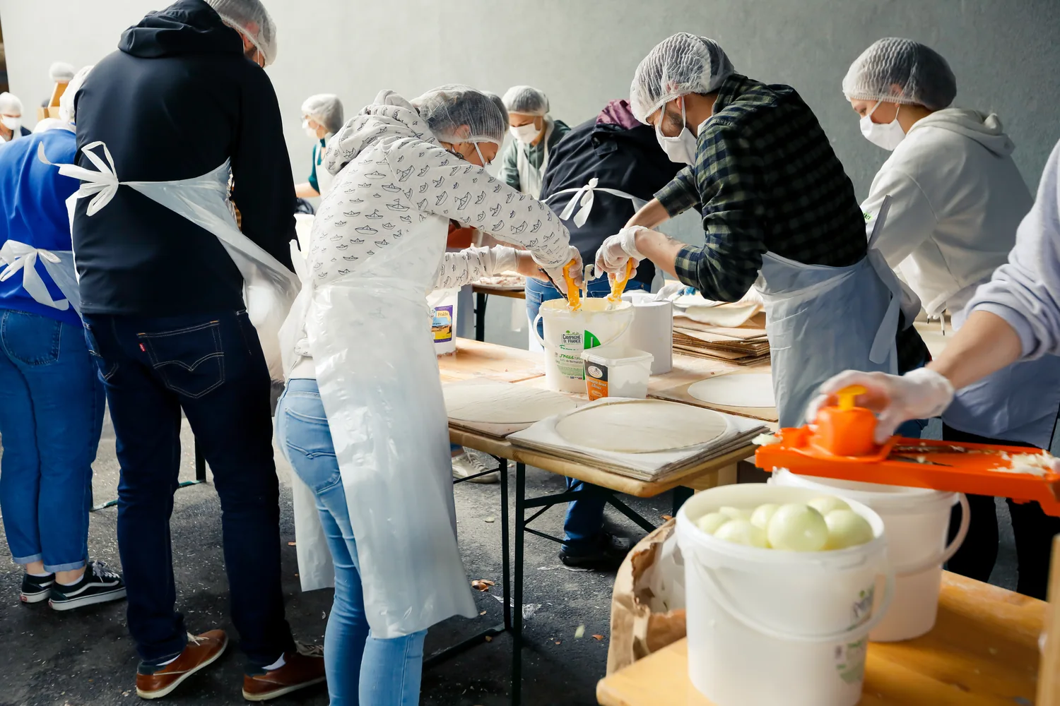 Des bénévoles masqués préparent les tartes flambées autour de grandes tables.